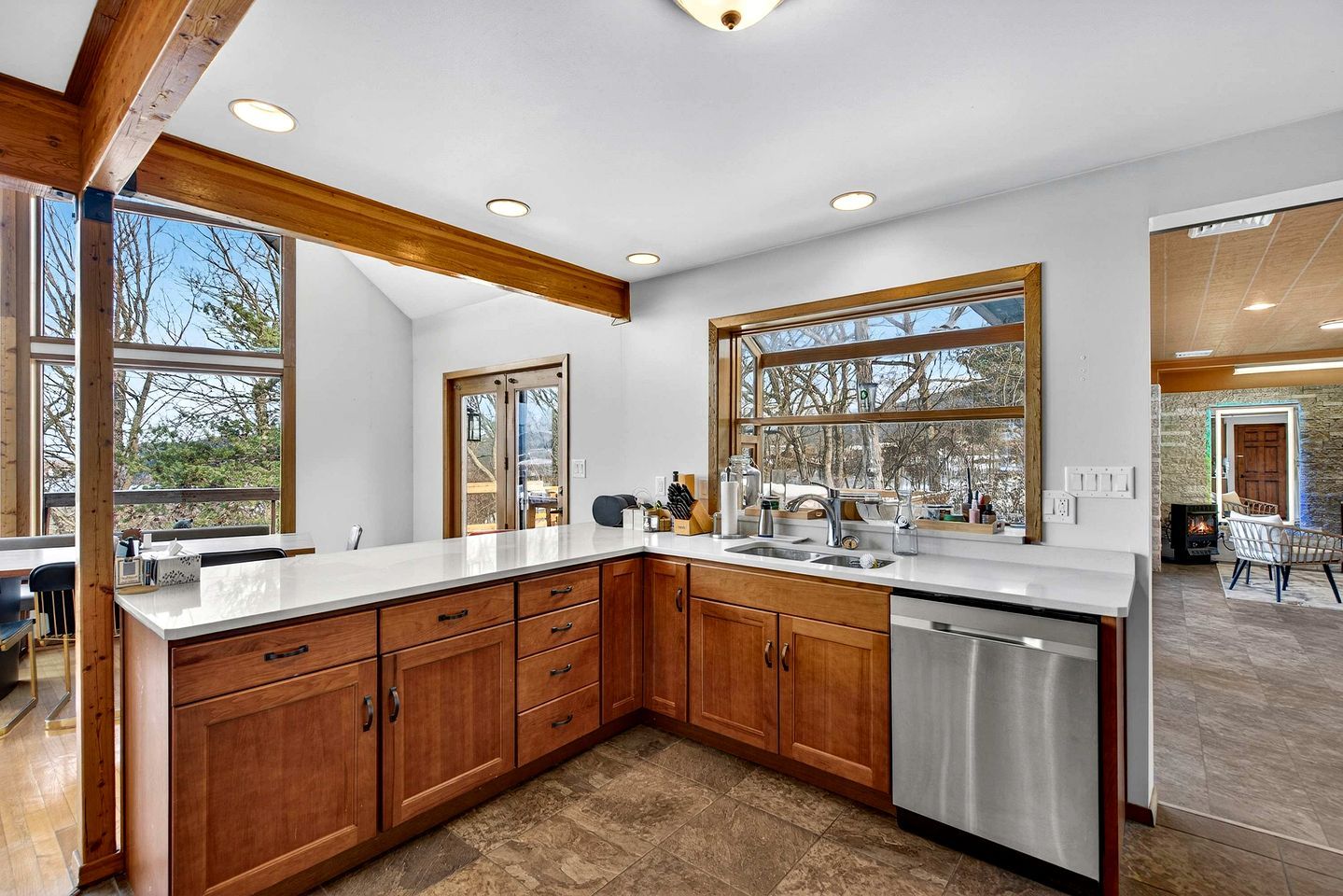 A modern kitchen with wooden cabinets, a stainless steel dishwasher, and large windows offering views of the outdoors.