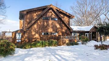 A wooden cabin with a sloped roof, a covered porch, and a snow-covered driveway.