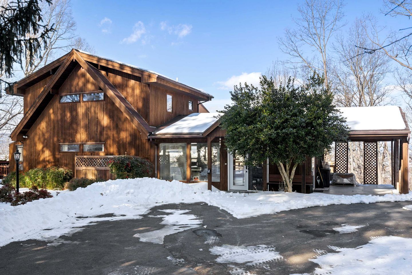 A wooden cabin with a covered porch and a snow-covered driveway.