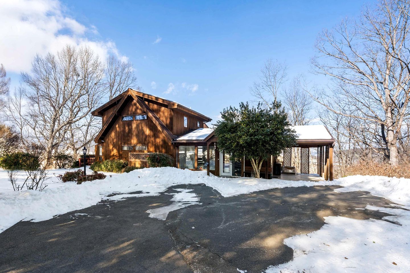 A wooden cabin with a snow-covered driveway and a covered outdoor seating area.