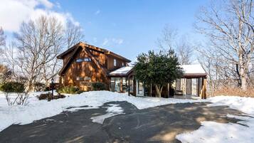 A wooden cabin with a snow-covered driveway and a covered outdoor seating area.