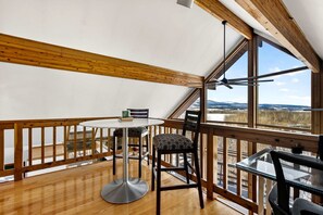 A room with a wooden ceiling, a round table, two chairs, and a view of a snowy landscape through large windows. - Modern Mountain Cabin with Hot Tub and Game Room Near Moorefield, West Virginia (Moorefield)