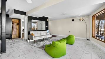 Una sala de estar moderna con un sofá, sillones de pelota verdes y un espejo grande, con vistas a través de una ventana.