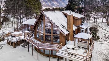 Eine Holzhütte mit einer Terrasse und einer überdachten Sitzgelegenheit im Freien, umgeben von Schnee und Bäumen.