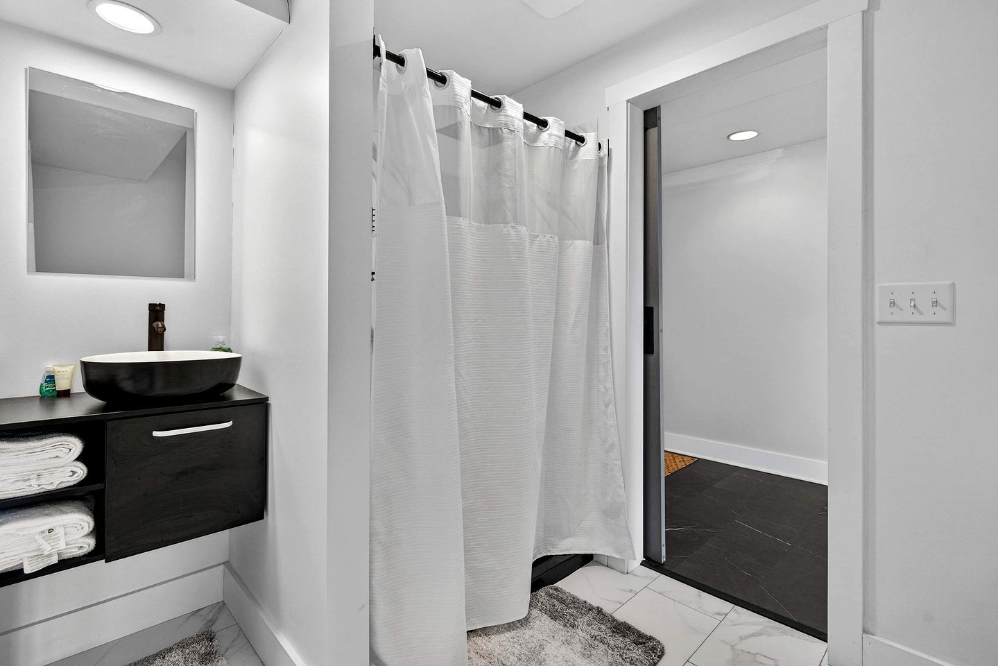 A modern bathroom with a black sink, white shower curtain, and a mirror above the sink.