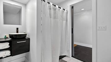 A modern bathroom with a black sink, white shower curtain, and a mirror above the sink.