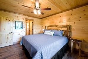 A wooden cabin bedroom with a bed, a ceiling fan, and a door. - Luxury Gatlinburg Cabin with Game Room & Hot Tub near Trolley in Gatlinburg, Tennessee (Gatlinburg)