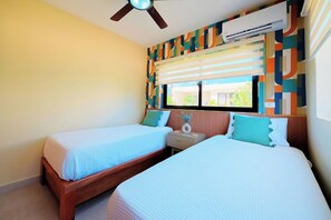 A hotel room with two beds, a ceiling fan, an air conditioner, a window with blinds, and a colorful wall pattern. - 2 Bed, Encuentro Retreat, Casa Tranquila (sosua)
