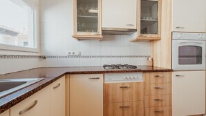 Una cuina amb armaris de fusta, forn integrat, rentaplats i una finestra.