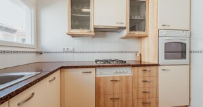 Eine Küche mit Holzschränken, einem eingebauten Backofen, einem Geschirrspüler und einem Fenster.
