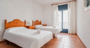Ein Zimmer mit zwei Betten, einem Holzkopfende, einem Nachttisch, einem Fenster mit Vorhängen und einer Tür.