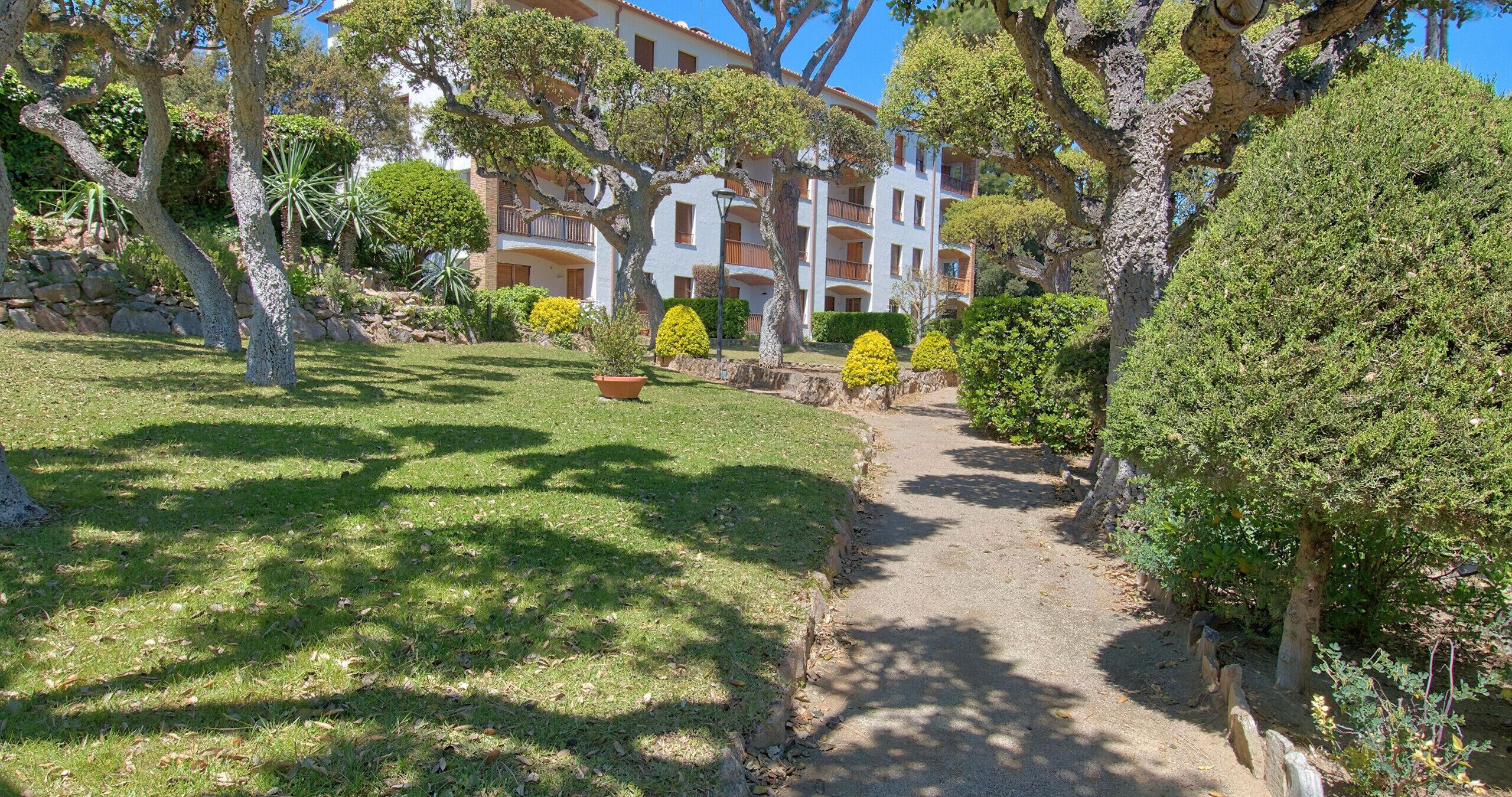 A pathway leading to a building with multiple balconies, surrounded by well-maintained grass and trees.