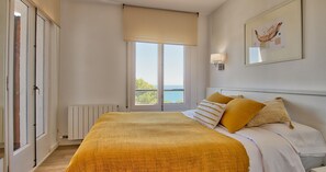 Ein Schlafzimmer mit Bett, Fenster mit Blick, Heizkörper und Wandleuchte.