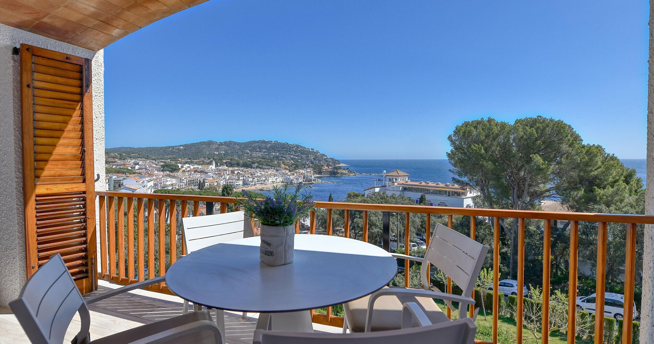 Un balcone con tavolo e sedie, vista su una cittadina costiera e il mare.
