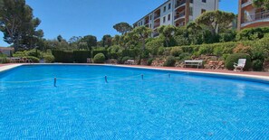 A swimming pool with a clear blue water surface, surrounded by a low stone wall and a hedge. - Renovated Sea View Apartment with Pool in Calella · Modern Design (Calella de Palafrugell)