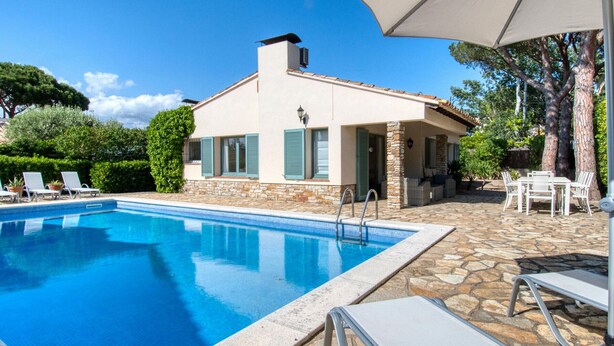 Una piscina con sillas de descanso, un patio de piedra y un edificio con contraventanas.