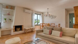 Una sala de estar con sofá, televisor, chimenea, mesa de comedor, sillas y una araña.