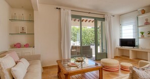 A living room with a glass coffee table, wicker furniture, a TV, and a sliding glass door leading to an outdoor area. - 4-Bedroom Villa with Pool in Calella · Ideal for Families (Calella de Palafrugell)