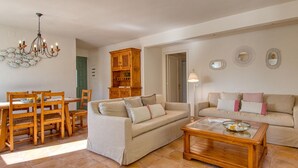 Una sala de estar con sofá, dos sillones, una mesa de centro, una mesa de comedor con sillas, una araña y un aparador de madera.