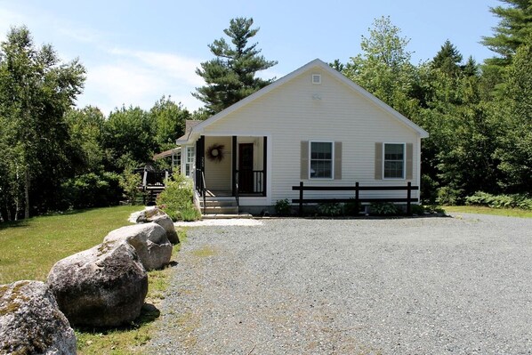 A single-story house with a front porch, a gravel driveway, and a wooden fence. - Spacious Ranch-Style Retreat with Private Deck, Nestled in Nature Near Acadia, Hancock Maine (Hancock)