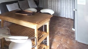 Een eetgedeelte met een houten tafel, stoelen, een bank, een wandklok, een decoratief gewei en een koelkast.