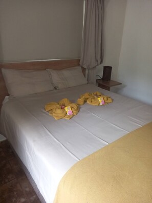 Uma cama com lençol branco, duas toalhas amarelas e uma pequena caixa sobre a cama.