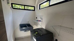 A compact kitchen with a built-in washing machine, a small sink, and two windows. - Tempátika Villa 3, New (Tempate)