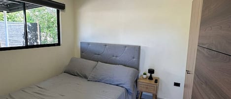 A bedroom with a bed, a nightstand, a window, and a door.