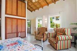Una habitación con una cama, dos sillones a rayas, techo de madera y vistas a zonas verdes.