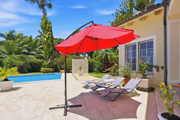 Zona de piscina con sillones de descanso y una sombrilla roja.