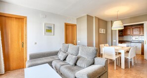 A living room with a grey sofa, a dining table with chairs, a kitchen area, and wooden doors. - 3-bedroom apartment 50m from the beach with parking (Calella de Palafrugell)