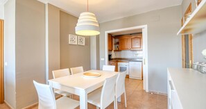 A modern kitchen with white cabinets, a dining table with chairs, and a hanging light fixture. - 3-bedroom apartment 50m from the beach with parking (Calella de Palafrugell)