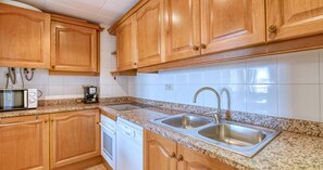 A kitchen with wooden cabinets, a microwave, a dishwasher, and a double sink. - 3-bedroom apartment 50m from the beach with parking (Calella de Palafrugell)