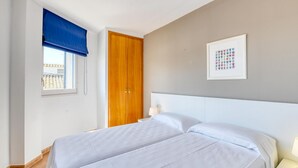 Ein Schlafzimmer mit einem Bett, einem Nachttisch, einem Fenster mit blauer Jalousie, einem Holzschrank und einem gerahmten Bild an der Wand.