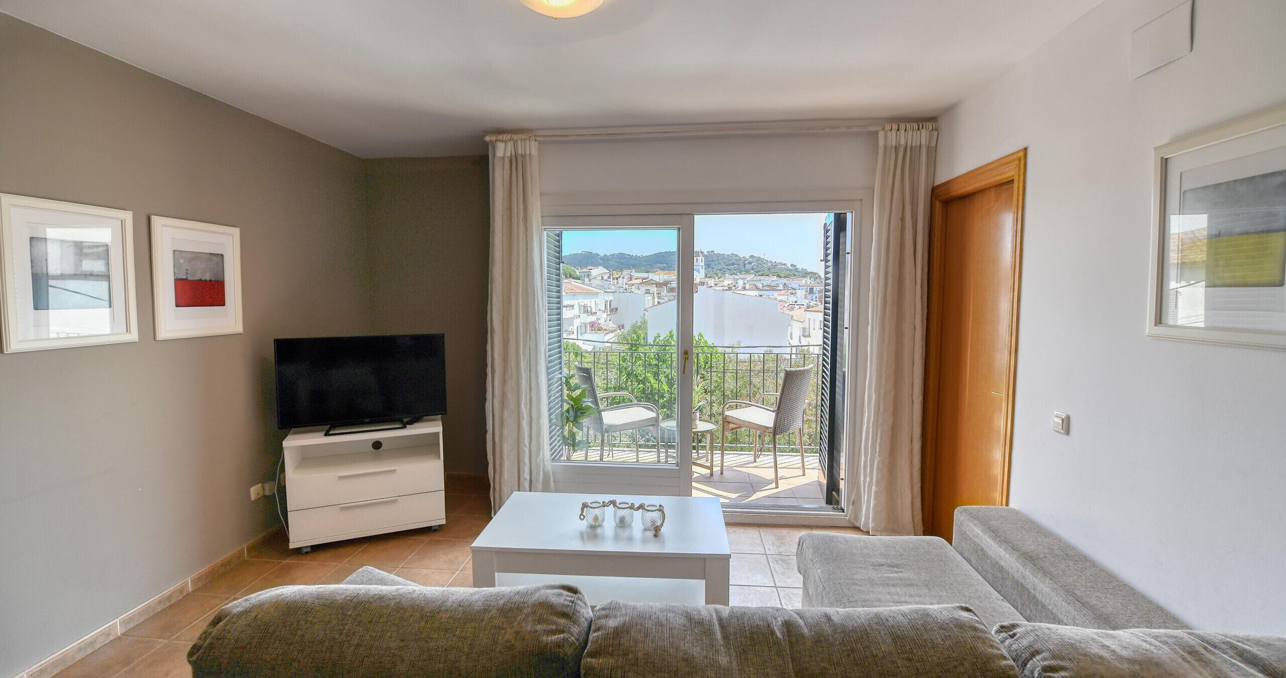 Ein Wohnzimmer mit einer Couch, einem Fernseher, einem weißen Couchtisch und einem Balkon mit Blick auf eine Stadt und Wasser.