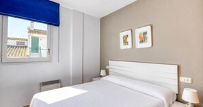 Ein Hotelzimmer mit einem Bett, einem Fenster mit blauer Jalousie, einer Wand-Klimaanlage und zwei gerahmten Bildern.
