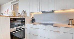 A modern kitchen with white cabinetry, a Bosch oven, a coffee maker, and decorative jars. - Modern three-bedroom apartment with pool in the center (Calella de Palafrugell)