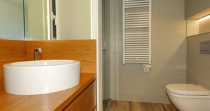 Uma casa de banho moderna com lavatório redondo, toucador de madeira, sanita e porta-toalhas fixado na parede.