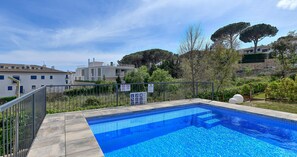 Piscina cercada por vegetação e edifícios, com grade de metal.