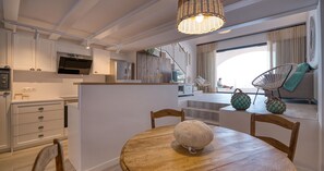 A modern kitchen with white cabinetry, a wooden dining table, and a hanging light fixture. - Seafront studio with sea views · Calella (Calella de Palafrugell)