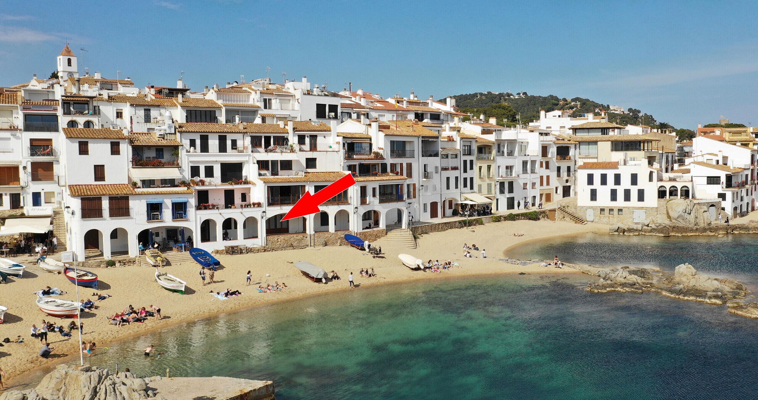 Une ville côtière aux bâtiments blancs, avec une plage de sable et des bateaux.