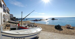 Eine Küstenlandschaft mit Booten, die an einem Sandstrand vor Anker liegen, einem wolkenlosen Himmel und einem Felsen im Wasser.