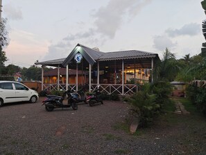 A building with a distinctive logo, a covered outdoor seating area, and a gravel driveway. - Mermaid Avisa (Arambol)