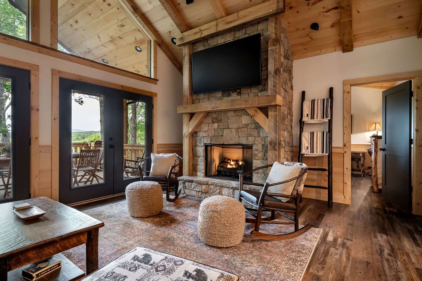 A cozy living room with a stone fireplace, wooden furniture, and a large TV mounted on the wall.