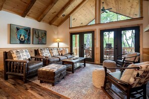 A cozy living room with a wooden ceiling, leather furniture, and large windows. - Luxury Mountain Cabin with Hot Tub, Sauna & Game Room Near Ellijay in Georgia (Ellijay)