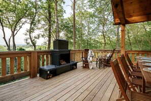 Een terras met een ingebouwde open haard, buiten zitplaatsen en uitzicht op het bos.