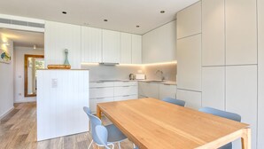 Een moderne keuken met witte kastjes, een houten eettafel en blauwe stoelen.