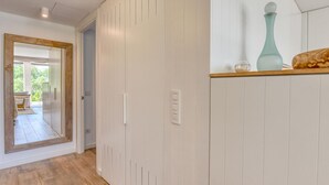 Een gang met houten vloer, witte muren, een spiegel met houten lijst en een deur naar een buitenruimte.