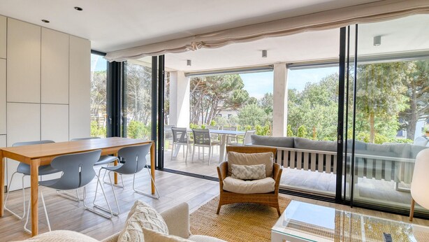 Een moderne woonkamer met een eethoek, grote ramen en een balkon met buitenmeubilair.