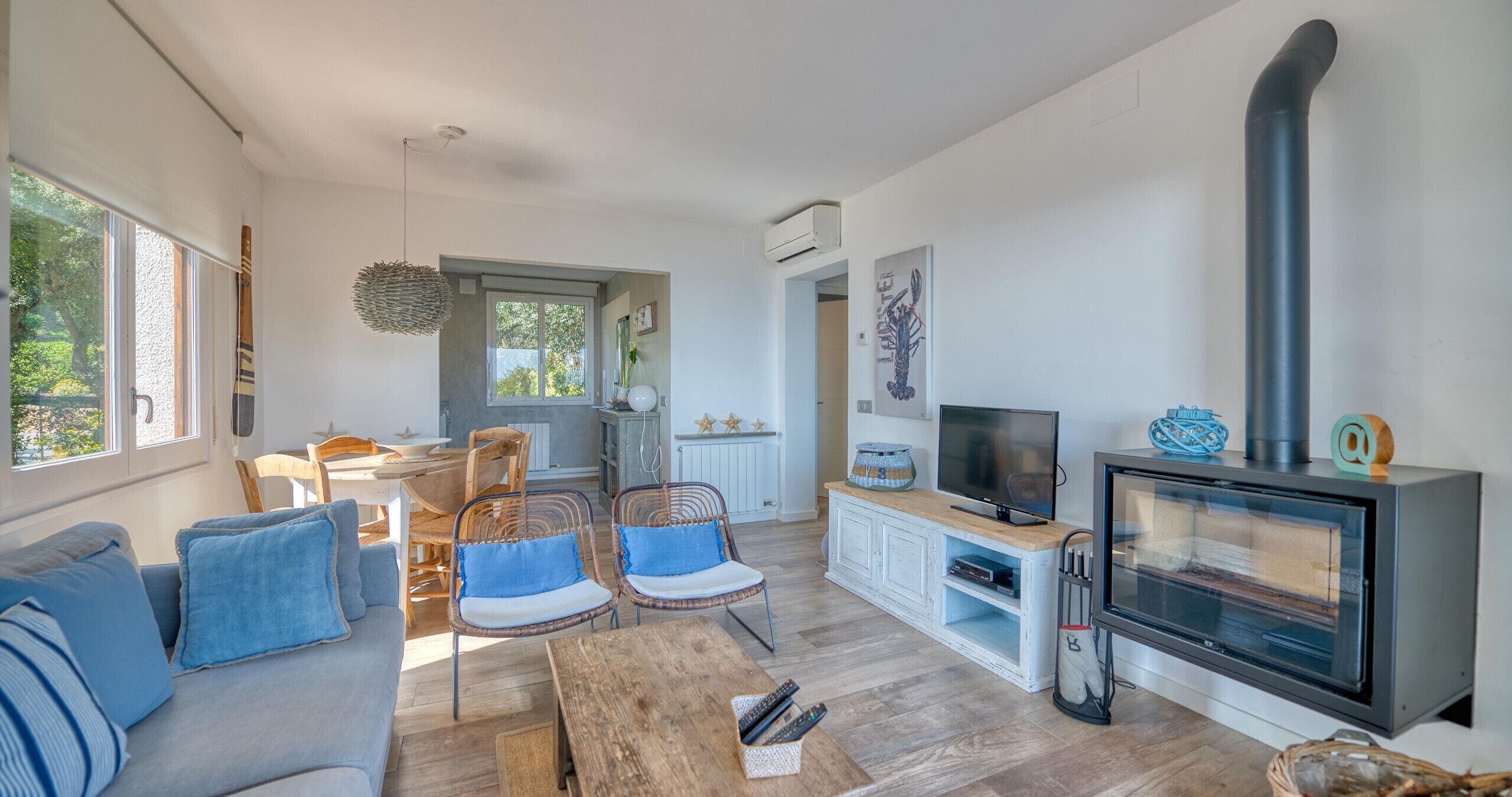 Een woonkamer met een bank, stoelen, een televisie, een open haard en een keuken op de achtergrond.